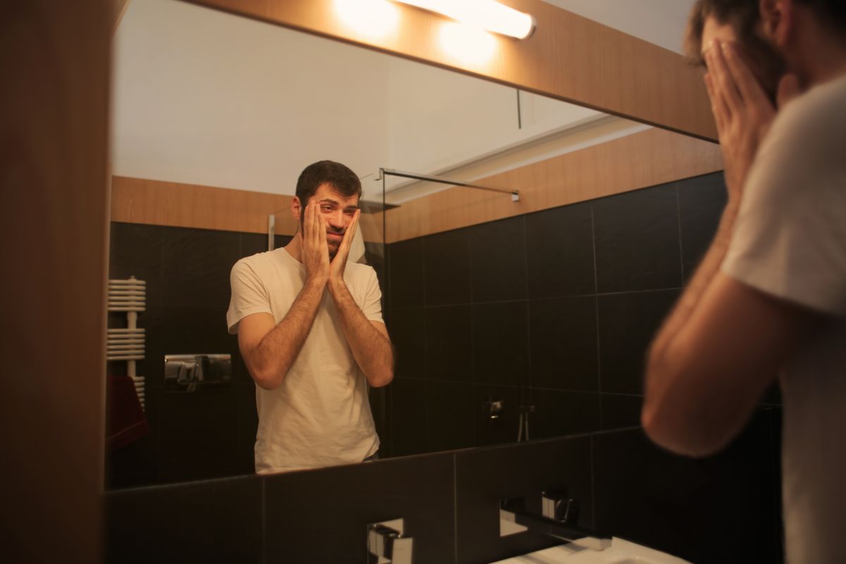 鏡の前で自分の生え際を確認する男性